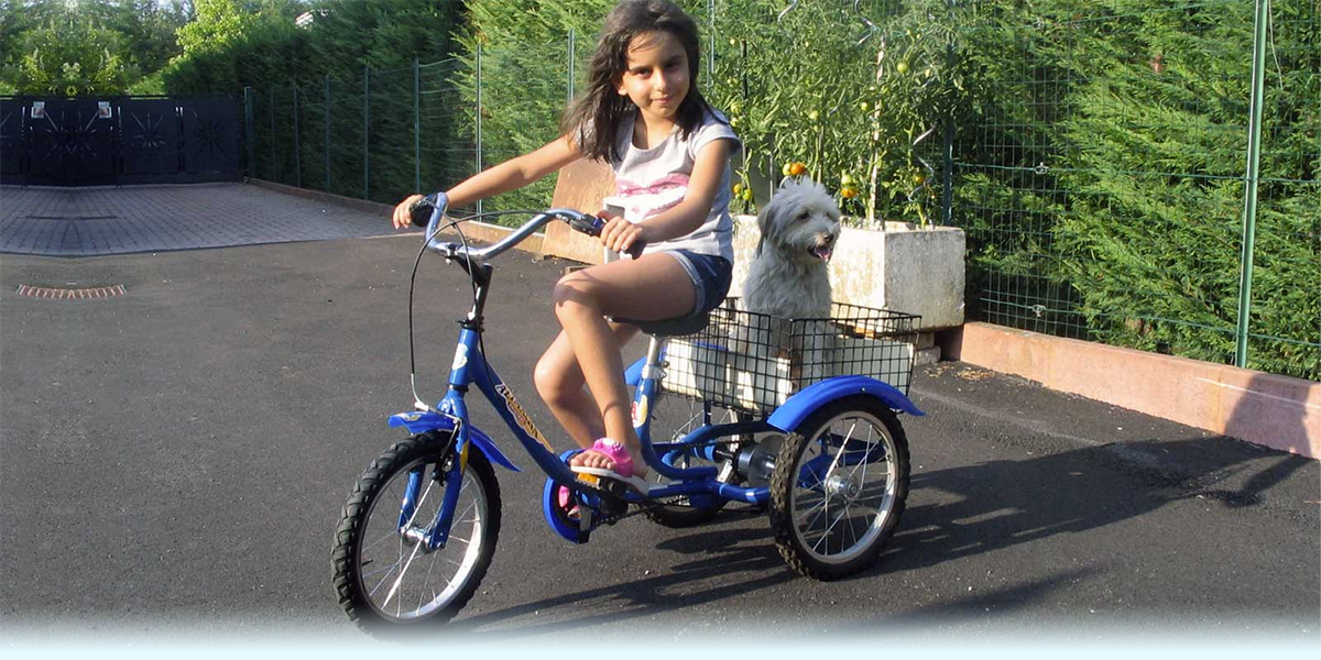 Bambina in sella al triciclo Vittoria blu, con il suo cane nel cestello